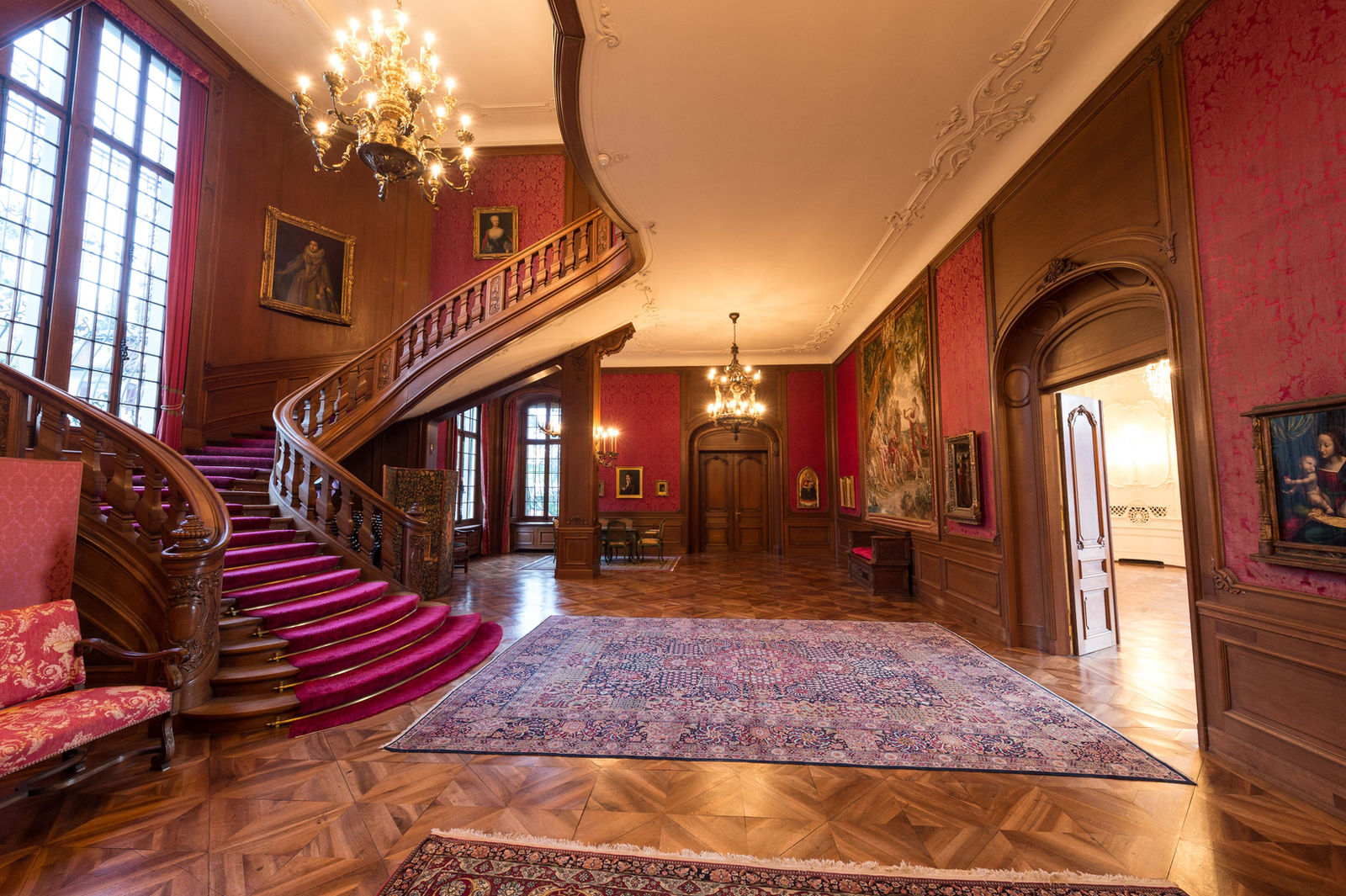 Grosses Foyer mit geschwungener Holztreppe und roten Wandbespannungen